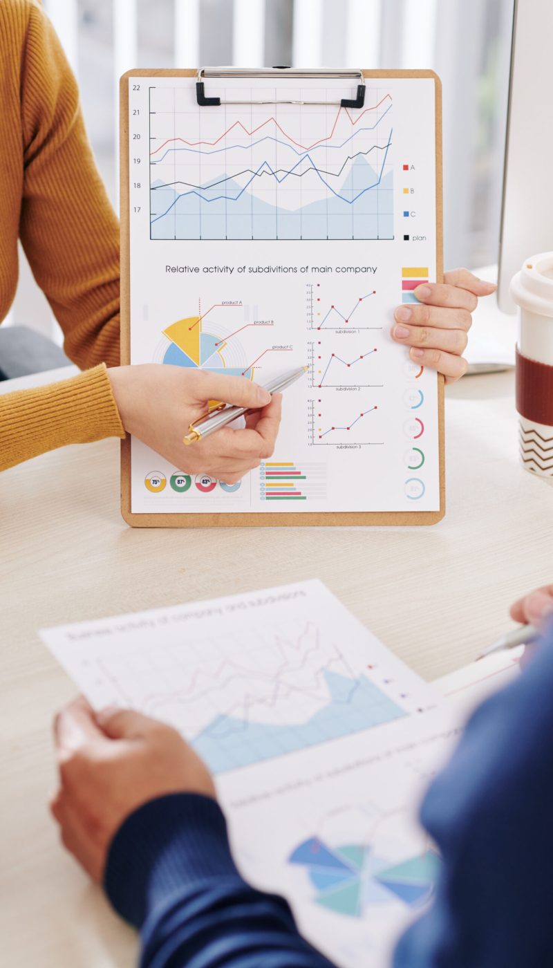 Cropped image of young businesswoman showing clipboard with financial chart and discussing information with colleague